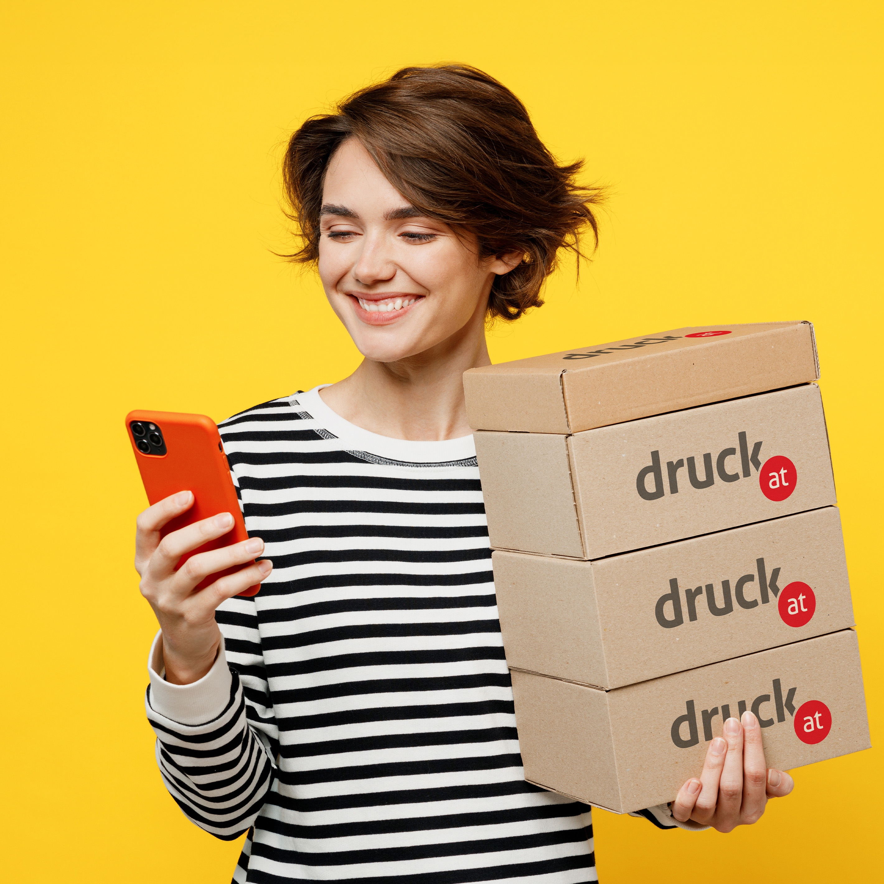 Zufriedene Frau mit bedruckten Paketen in der einen Hand und einem Smartphone in der anderen 