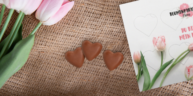 Schokoherzen und bedruckte Kartonschachtel liegend auf Tisch neben rosa Tulpen
