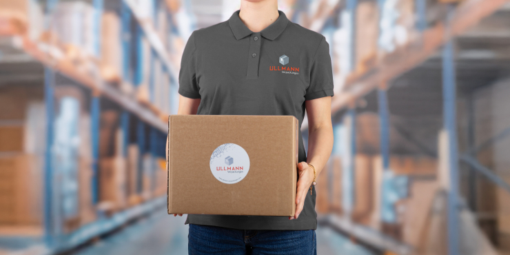 Frau hält einen Karton mit einem Sticker in den Händen und steht in einem Lager