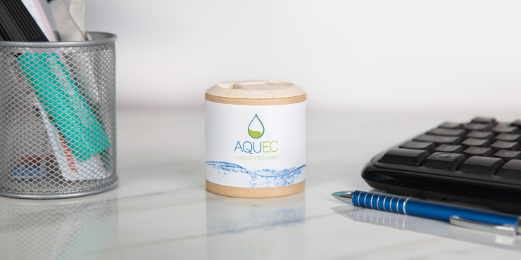 Bedruckte Werbedose gefüllt mit Kaugummi steht auf einem Schreibtisch zwischen Stiftbecher und Tastatur, davor liegt ein blauer Kugelschreiber