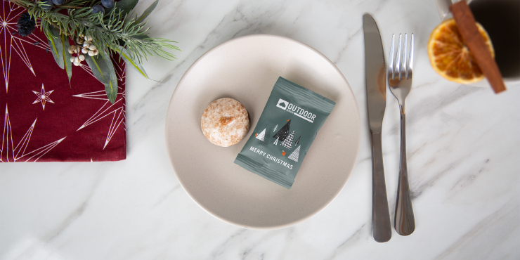 Lebkuchen in bedruckter Verpackung auf einem weißen Teller liegend daneben ein Besteck und weihnachtliche Dekoration