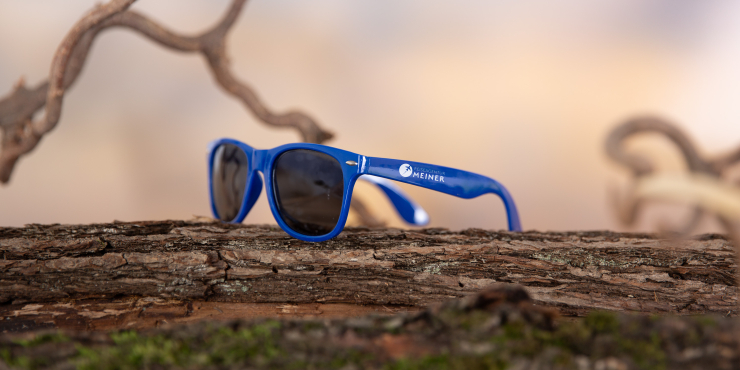 Dunkelblaue Sonnenbrille mit Aufdruck auf Baumstamm