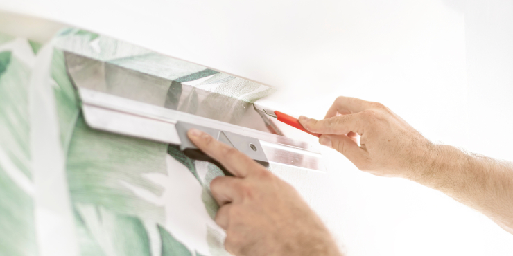 Mit Tapetenschaber und Tapetenmesser wird die Tapete festgedrückt und abgeschnitten