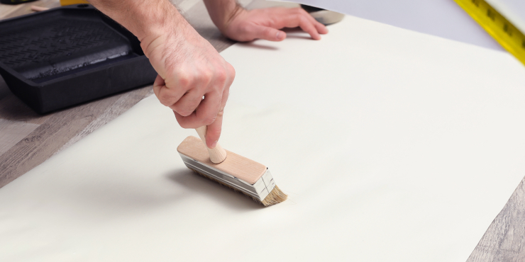 Mann trägt auf der Rückseite der Tapete den Tapetenkleister mit einem Pinsel auf