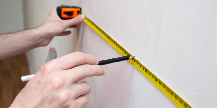 Mann zeichnet mit Maßband und Bleistift die Position der Tapete an
