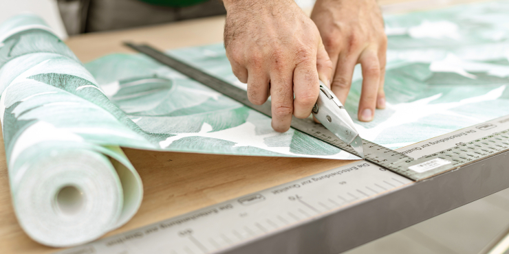 Bedruckte Tapete wird mit Tapetenmesser und Lineal zugeschnitten