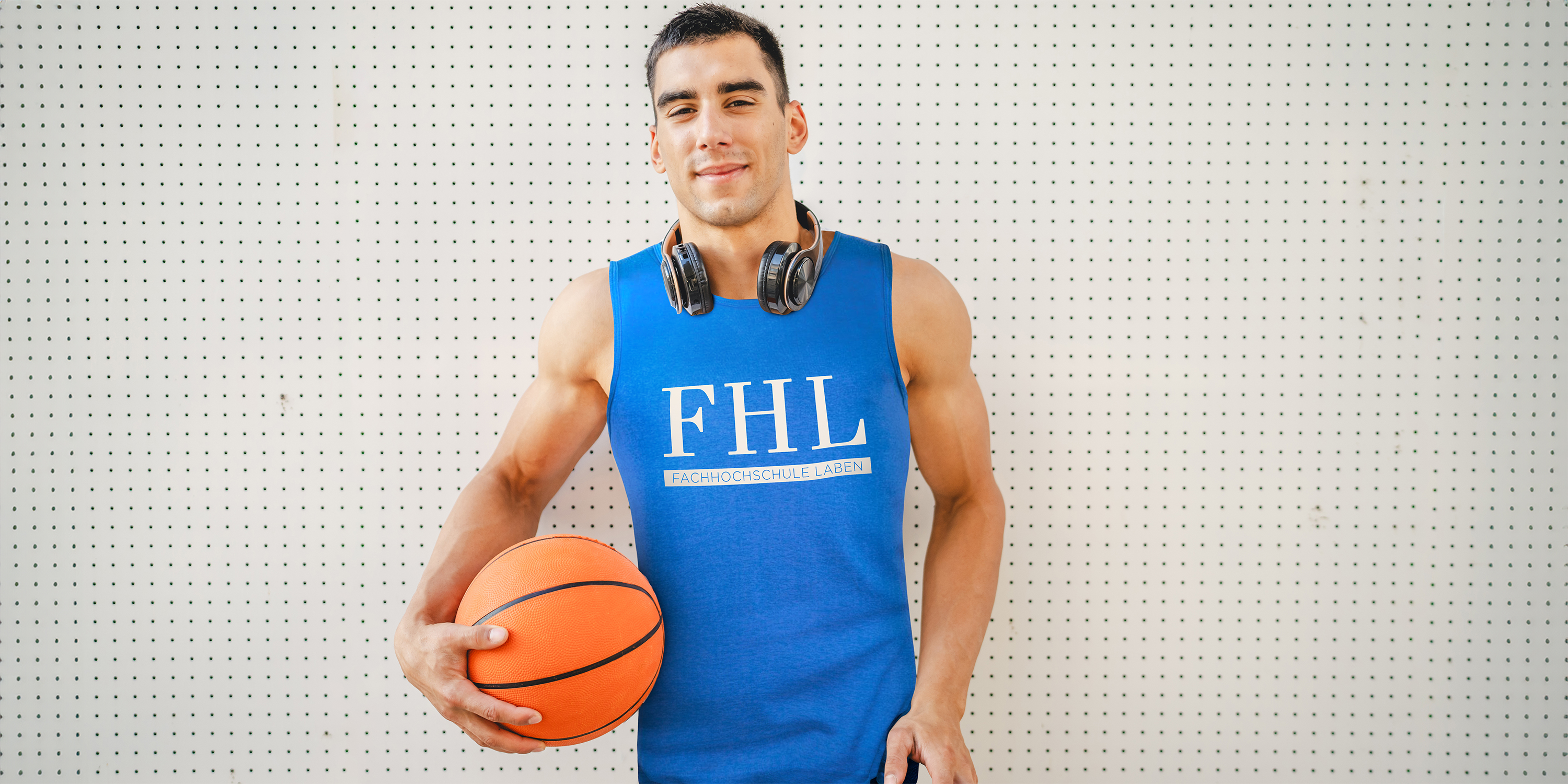Junger Mann hält Basketball in der Hand und trägt ein ärmelloses T-Shirt mit dem Druck einer Mannschaft
