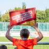 Ein Junge hält ein Anfeuerungsschild von druck.at hoch und feuert beim BFC an