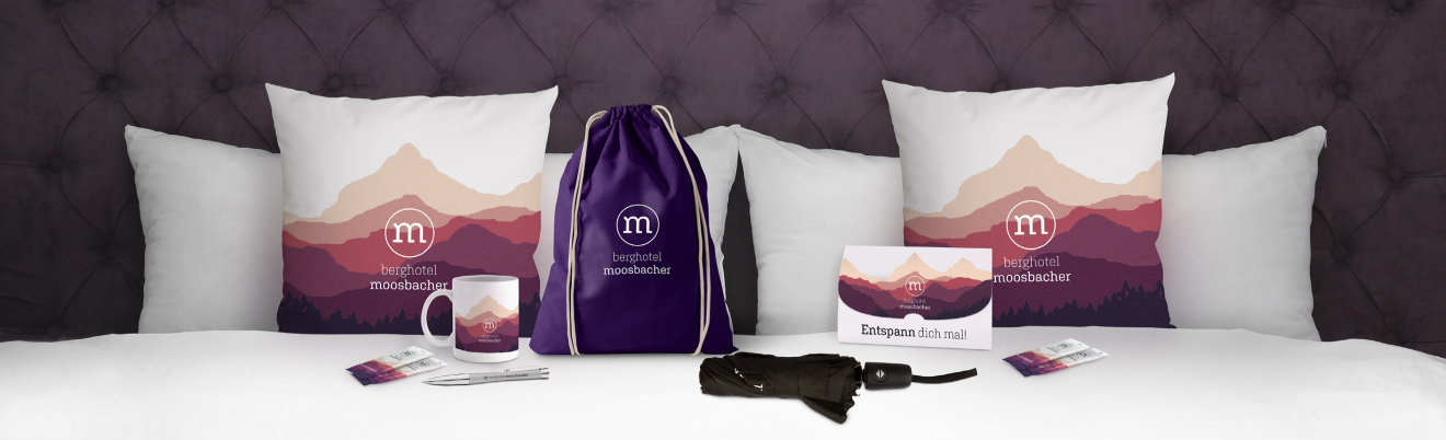 Mit dem Logo bedruckte Polster und Snacks auf einem Bett im Hotelzimmer