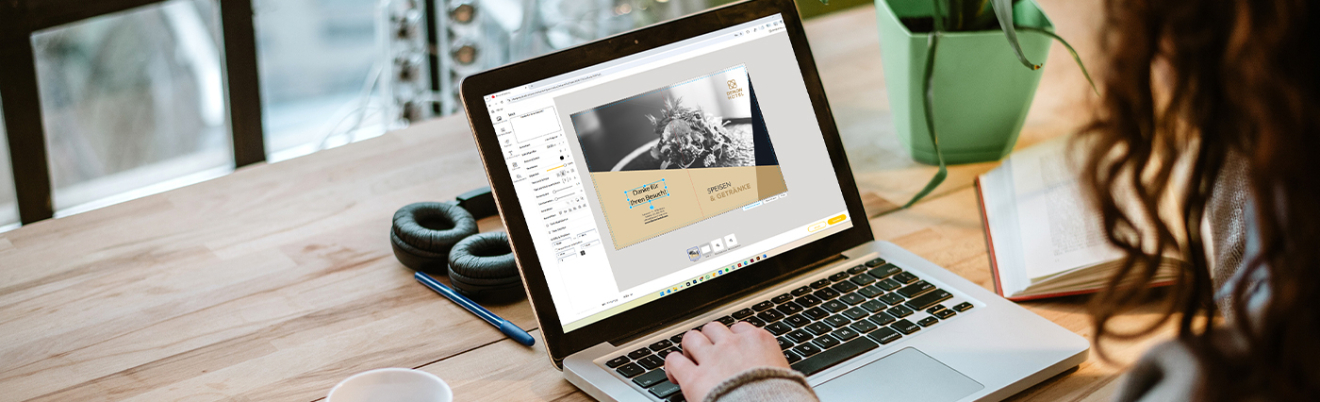 Person sitzt mit einem Laptop am Schreibtisch und gestaltet ein Design im Online-Designer
