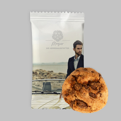 Ein Schokoladenkeks neben einer individuell gestalteten Verpackung auf grauem Hintergrund