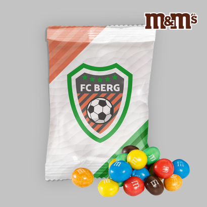 M&amp;Ms liegen neben bedrucktem Flowpack auf grauen Hintergrund