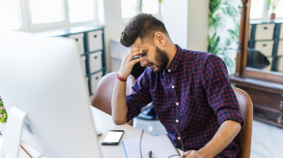Ein Mann sitzt am Schreibtisch und hält sich die Hand vor sein Gesicht