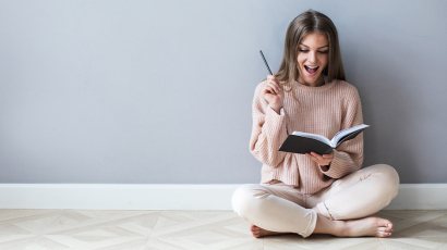 Eine Frau sitzt am Boden, lehnt an der Wand und liest ein Buch.