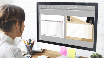 Eine Frau sitzt vor einem Bildschirm. Auf diesem sind zwei Kalenderseiten in Adobe InDesign geöffnet.