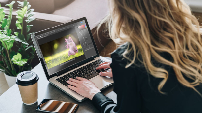 Eine Frau schaut in einen Laptop hinein, auf dem Photoshop geöffnet ist.