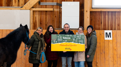 Bild von der Übergabe des Spendenschecks mit dem Speicher der Photovoltaikanlage im Hintergrund