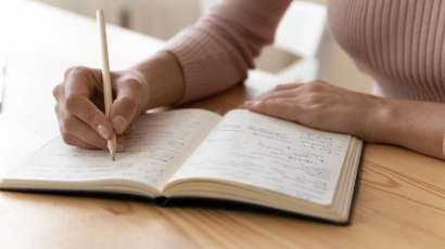 Eine Person schreibt mit einem Stift in ein Notizbuch.