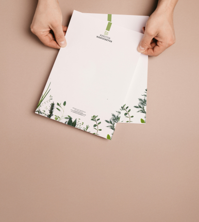 Person hält zwei personalisierte Briefpapier-Seiten in der Hand vor einem hellbraunen Hintergrund