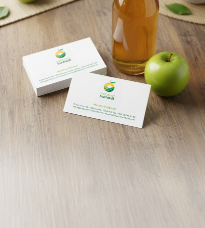 Klassische Visitenkarten mit individuellem Design und in Kleinmenge stehen neben einem Apfel und einer Flasche Apfelsaft auf einem Tisch