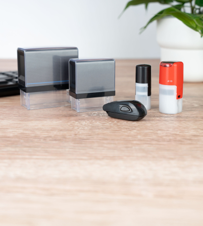Verschiedene Colop-Stempel im individuellen Design stehen auf einem Bürotisch neben einer Grünpflanze