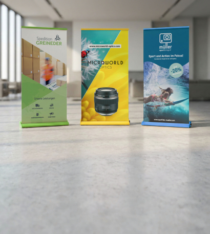 Drei bedruckte Color-Roll-ups stehen in einer Messehalle