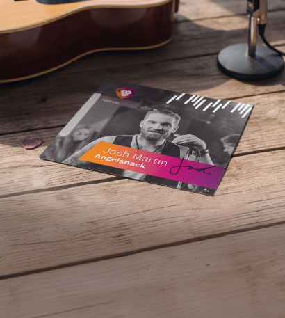Bedruckte Autogrammkarten liegt auf einem Holzuntergrund neben einer Akustikgitarre und einem Mikrofonständer