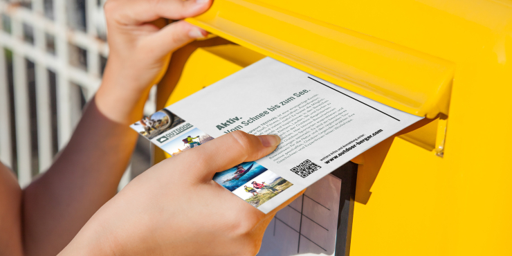 Jemand wirft bedruckte Postkarte in einen Postkasten