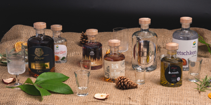 Verschiedene individuell gestaltete Spirituosenflaschen und Gläser auf Jutestoff mit Naturdekoration