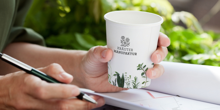 Jemand schreibt und hält einen bedruckten Becher