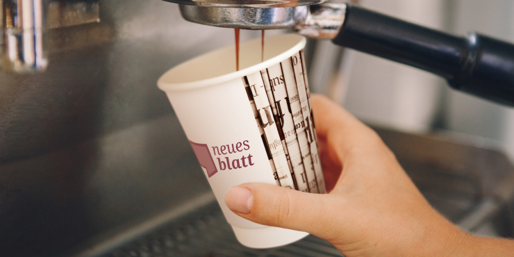 Jemand nimmt sich Kaffee mit bedrucktem Becher