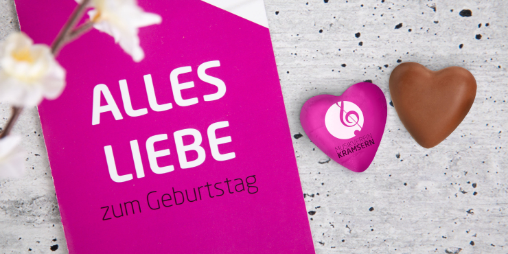 Schokoherz mit und ohne personalisierte Verpackung liegen auf Betonuntergrund neben einer Karte 
