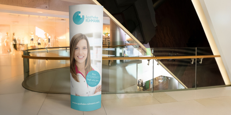 Ellipsenaufsteller mit individuellem Logo steht in einem Einkaufszentrum bei einem Stiegenaufgang