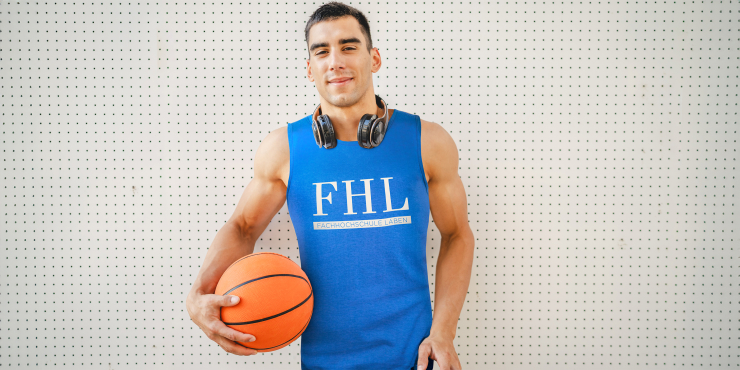 Mann mit Basketball trägt ärmelloses T-Shirt mit Logo des Teams