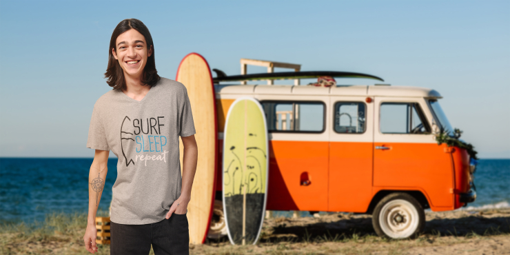 Junger Mann trägt individuell bedrucktes T-Shirt und ist mit dem Camper und seinem Surfbrett unterwegs