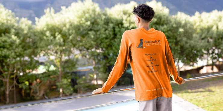 Mann steht an Balkon und trägt ein langarm T-Shirt, welches am Rücken bedruckt ist
