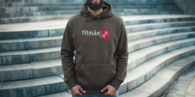 Männliche Person steht vor einer Treppe und trägt einen dunkelgrauen Hoodie mit Bauchtasche, der ein Logo auf der Vorderseite aufgedruckt hat