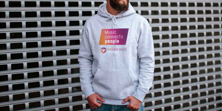 Männliche Person steht vor Absperrung und trägt einen hellgrauen Fruit of the Loom-Hoodie mit Bauchtasche und Logo auf der Brust aufgedruckt