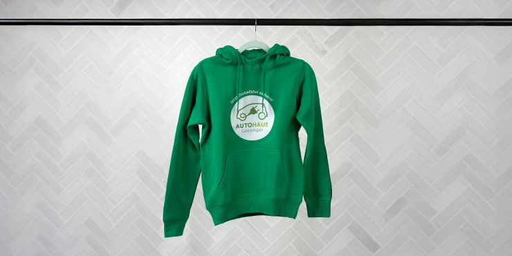 Grüner Hoodie von Printer mit Logo aufgedruckt auf der Vorderseite hängend auf einer schwarzen Kleiderstange