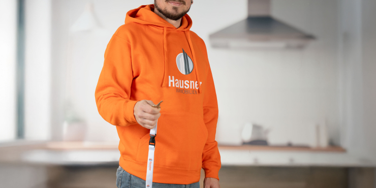 Immobilienmakler im orangenen Russell™-Hoodie, bedruckt auf der Vorderseite, übergibt den Wohnungsschlüssel