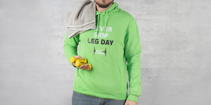 Mann im Fitnessstudio trägt Hoodie mit Bauchtasche in der Farbe Lime mit einem Logo-Aufdruck auf der Vorderseite
