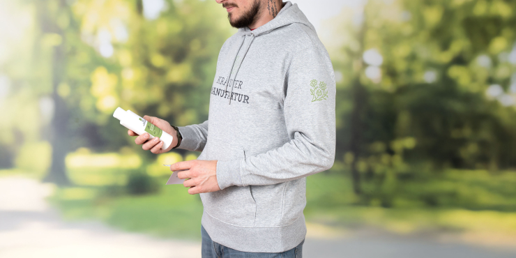 Männliche Person steht im Garten und trägt einen grauen Stanley/Stella-Hoodie mit Aufdruck an der Brust und an den Ärmeln