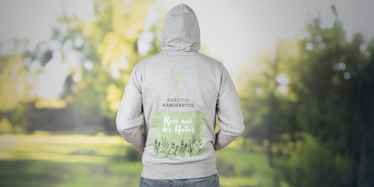 Männliche Person steht im Garten und trägt einen grauen Stanley/Stella-Hoodie mit Druck am Rücken