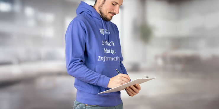 Mann im dunkelvioletten Cruiser Hoodie mit aufgedrucktem Logo auf der Brust steht im Raum und nimmt Notizen