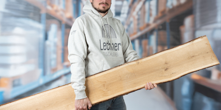 Mann steht im Lager, hält ein Holzbrett und trägt einen naturweißen Stanley/Stella-Hoodies mit vorderen Logo