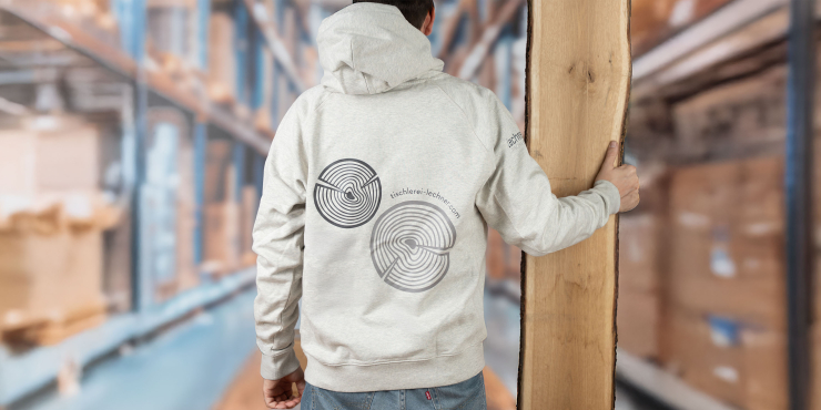 Mann steht im Lager, hält ein Holzbrett und trägt einen naturweißen Stanley/Stella-Hoodies mit Logo am Rücken