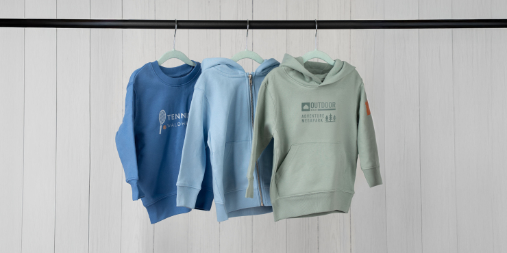 Kobaltblauer Sweater, hellblauer Zip-Hoodie und mintgrüner Hoodie mit bedrucktem Logo hängen auf einer Stange