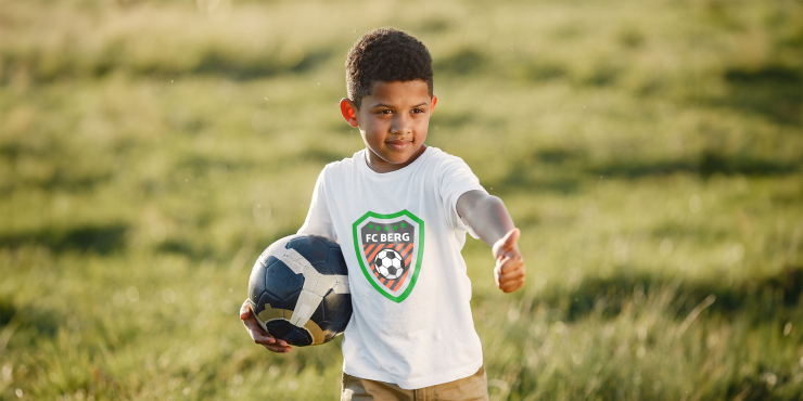 Bub spielt Fußball und trägt ein mit dem Logo des Vereins bedrucktes T-Shirt