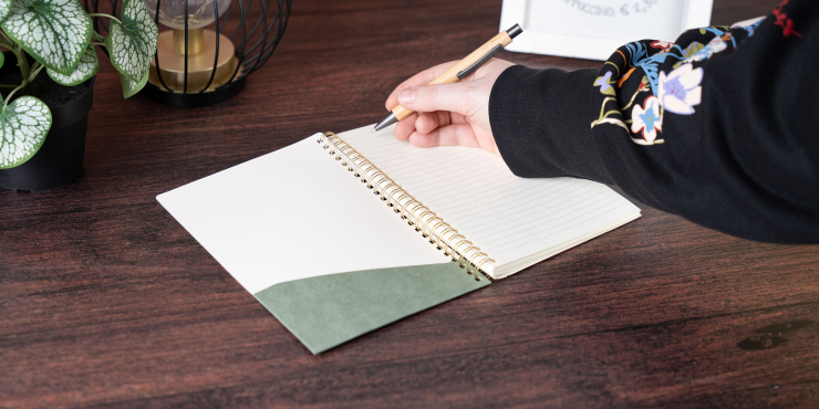 Person schreibt mit einem Kugelschreiber im personalisiertem A5-Notizbuch im Hochformat