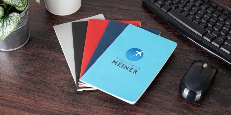 Personalisierte Rime A5-Notizbücher in verschiedene Farben liege gefächert auf einem Tisch neben einer Grünpflanze und einer Tastatur